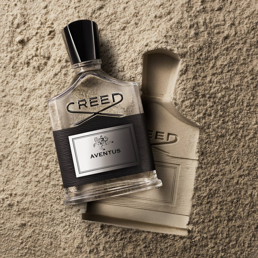 Creed Aventus eau de parfum flacon resting on a textured stone surface